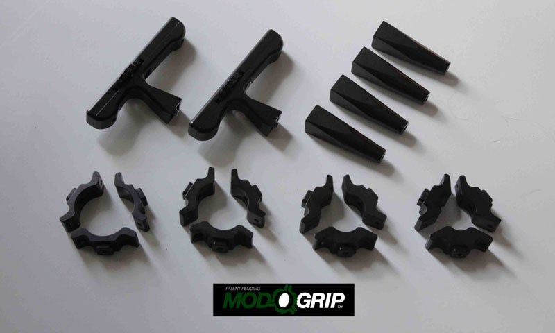 Black plastic parts with various shapes and sizes on a white surface, MOD GRIP logo in green and white.