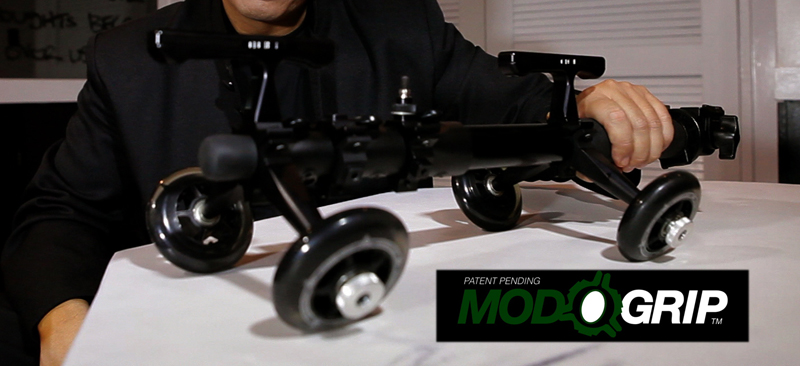 A man holds a precision work device with wheels on a white table, near the ModoGrip logo.