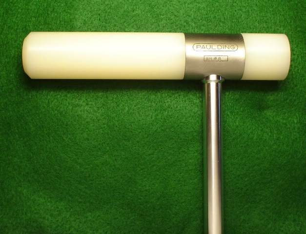 A cylindrical tool handle with light beige color and a long silver metal shaft extending to the right side.
