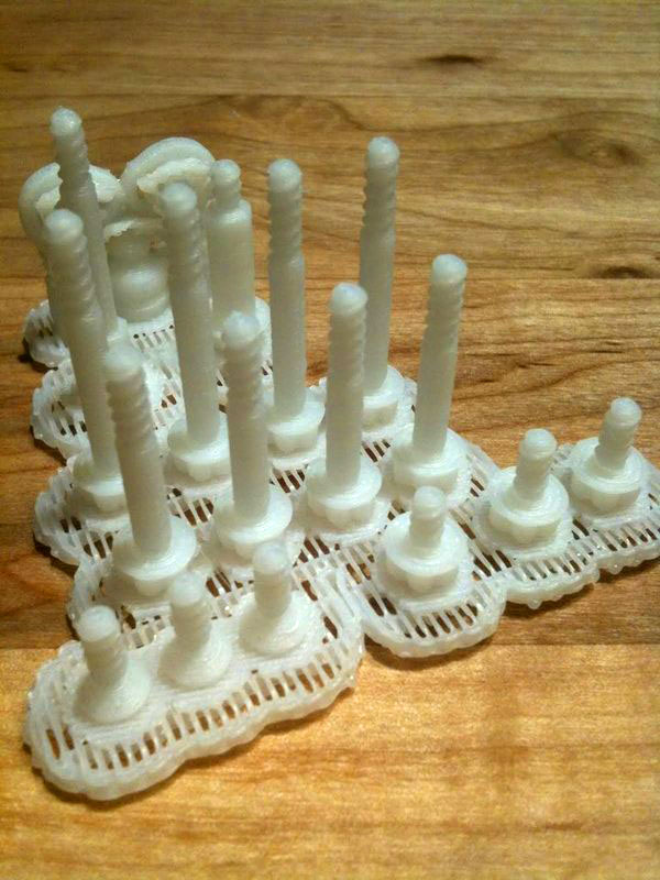 White 3D printed objects with cylindrical protrusions arranged in a grid-like pattern on wood.