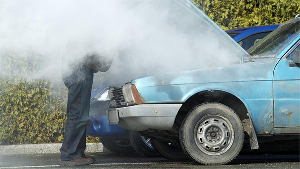 Blue car with smoke under hood, parked on urban road.