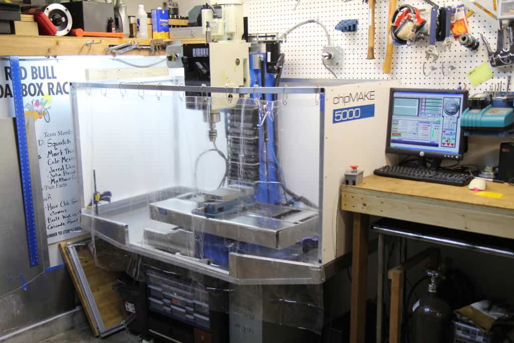 White CNC milling machine with chipMAKE 5000 label, clear plastic enclosure and blue column.