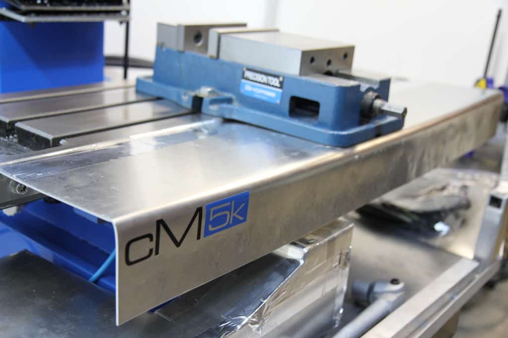 Large metal machine with prominent "CM5K" logo in industrial workshop setting.