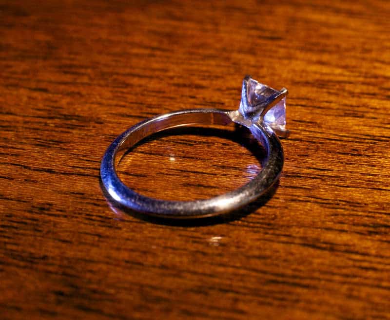 Silver ring with diamond or gemstone on dark wood grain surface.