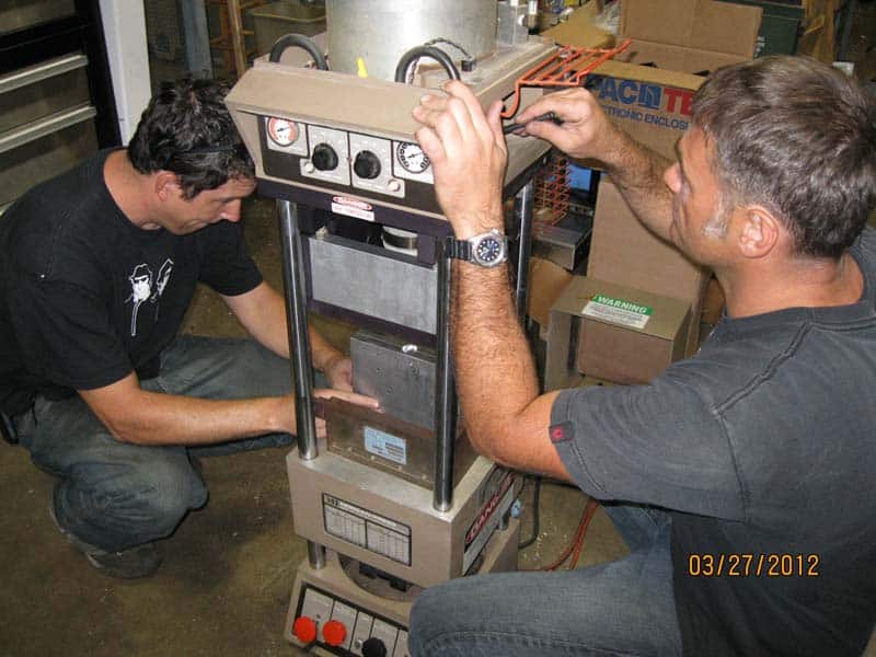 Two men working together on an industrial device in a workshop or manufacturing setting.
