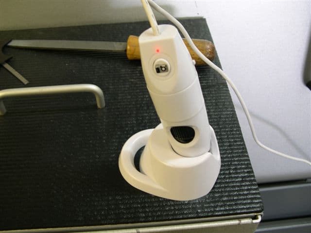 A digital microscope with a white body and red light on its top, placed on a black surface.