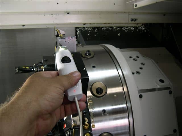 A white digital microscope with black lens cap and red light on a workbench with scattered debris and metal components.