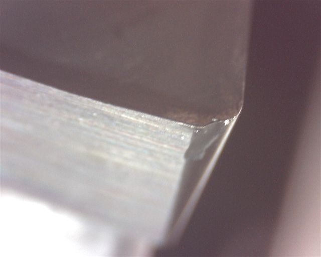 Sharp metal tool or blade edge, smooth and flat surface under magnification.