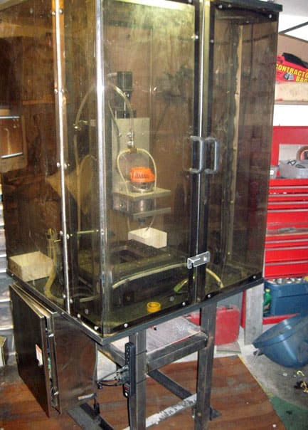 Transparent glass enclosure with metal components and black base, featuring a lathe or milling machine inside.