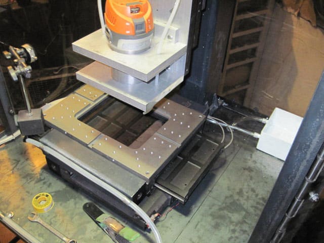 Milling machine with orange and silver tool on black base plate over gray table.