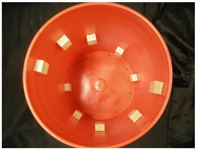 Large orange plastic bucket with holes, used for tumbling parts.