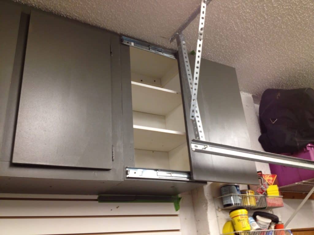 A sliding door cabinet in a garage workshop setting with gray doors and three shelves.