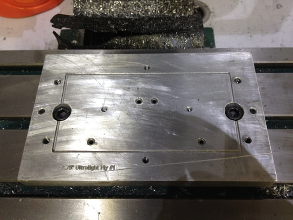 A rectangular silver metal plate with multiple holes of varying sizes on a flat surface.