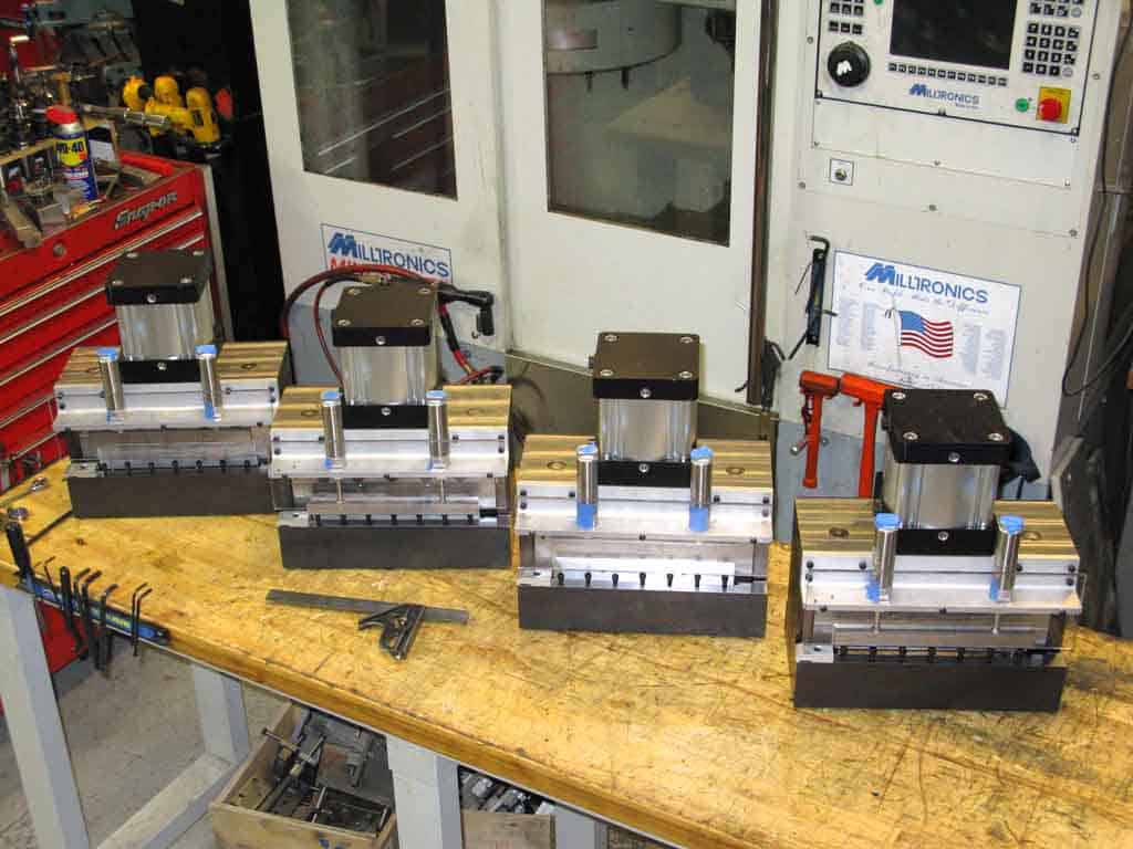 Precision die-cutting devices on a wooden workbench in a machine shop, featuring metal components and adjustment knobs.
