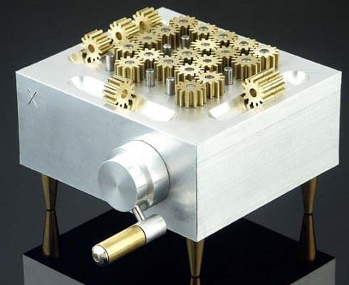 Silver gear box with brass gears on wooden legs against a dark background.