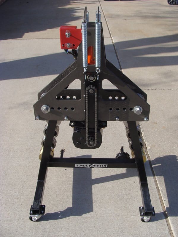 Black metal device with red component and two long springs, on a concrete surface.