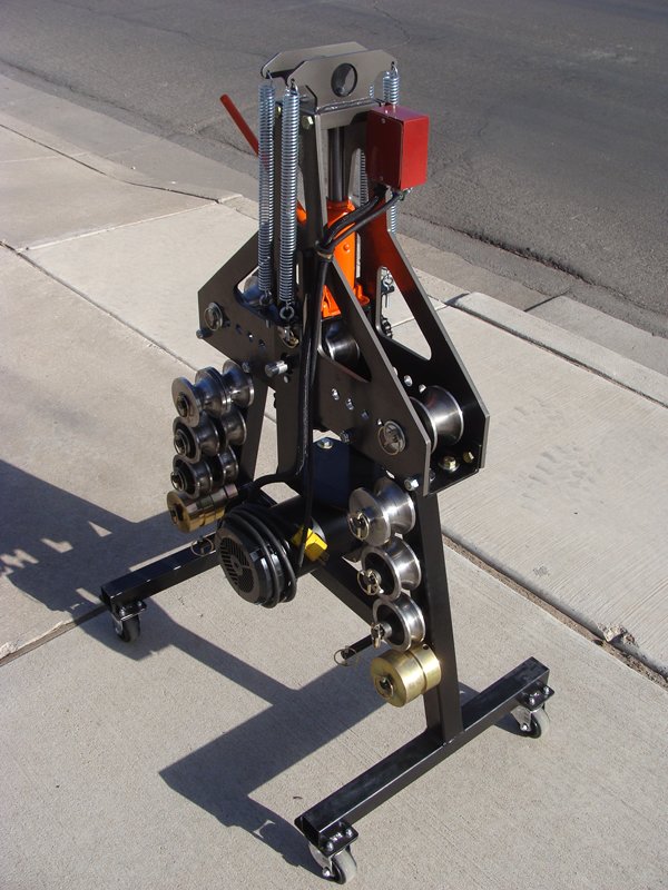 Black metal stand with wheels on concrete surface holding collection of mechanical parts in various shapes and sizes.