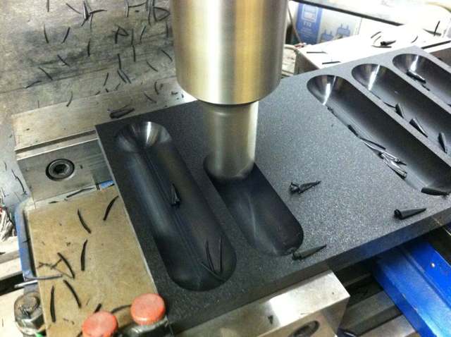 Black metalworking toolpost garter with curved grooves and small holes.