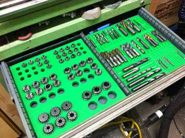 A green tray filled with various metal parts and tools in a machining setting.