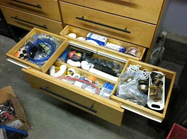 Wooden drawer with various tools and supplies in a workshop setting.