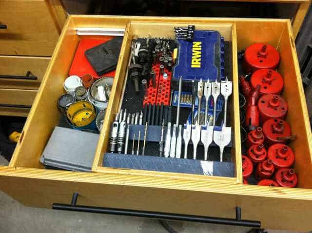 Wooden drawer filled with clamps, wrenches, and machinery parts organized into separate compartments.