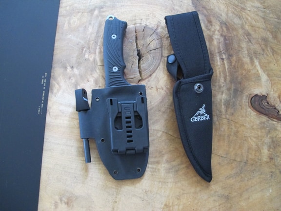 A Gerber knife with black sheath and belt clip on a light-colored wooden surface.
