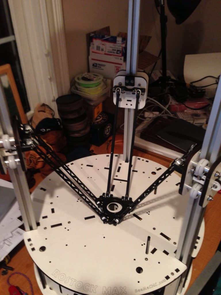 A 3D printer or CNC machine on a cluttered workshop table, surrounded by tools and materials.