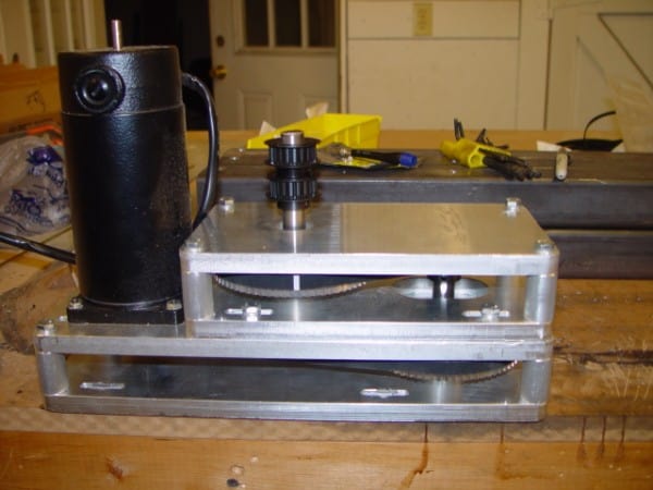 A 4th axis gearbox made of aluminum with a black motor on a workbench.