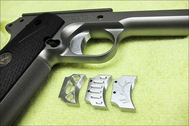 Silver metal 1911 pistol trigger shoe with intricate design and craftsmanship.