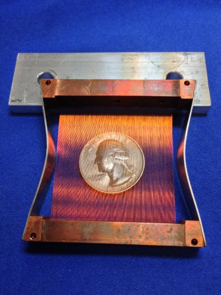 Copper-colored metal device with a coin affixed to its center, set against a blue background.