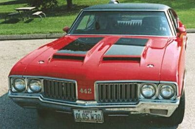 Red 1970 Oldsmobile 442 with black stripes on hood and "OLDS V30" license plate.