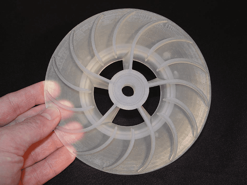 A circular object with a central hole, created using 3D printing or laser sintering, with curved lines and ridges on its surface.