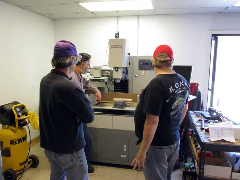 Four individuals gathered around a large industrial machine in a workshop setting.