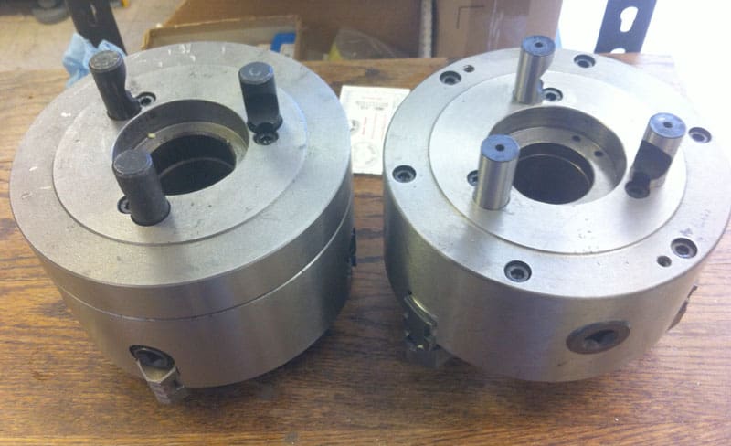 Two large metal components with central holes and protruding black rods on a wooden surface.