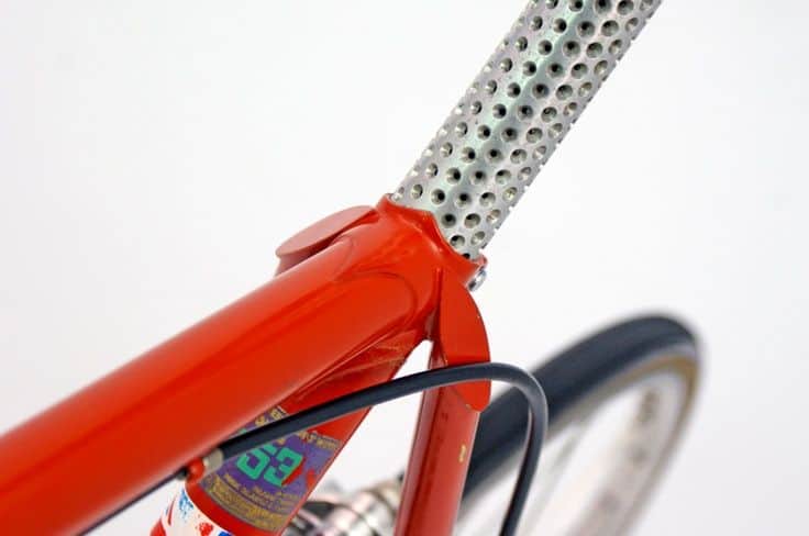 Red metal bicycle frame head tube with distinctive hole pattern.