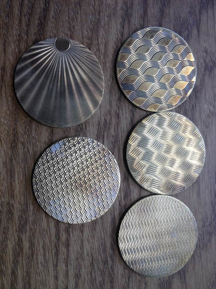 Intricate guilloche-patterned metal discs on dark wood background.