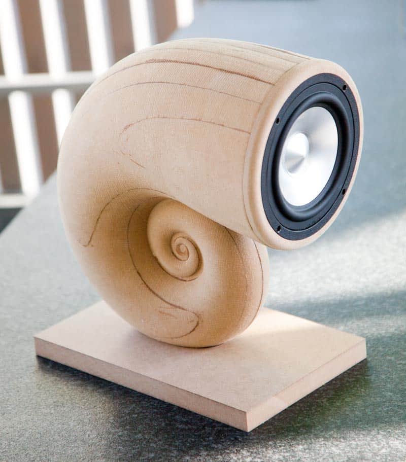 Wooden speaker resembling a snail shell in natural finish.