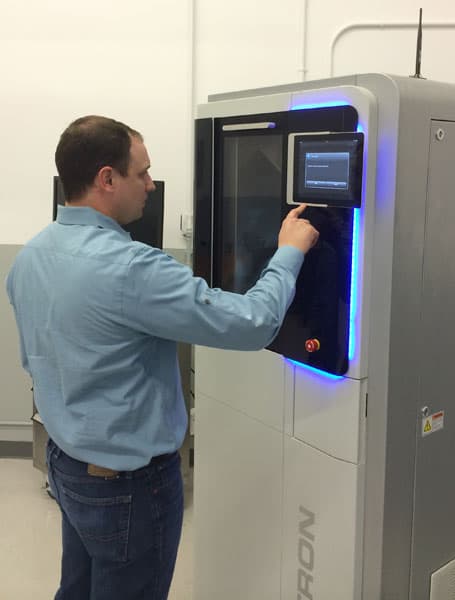 Man standing in front of CNC machine with glowing blue screen.