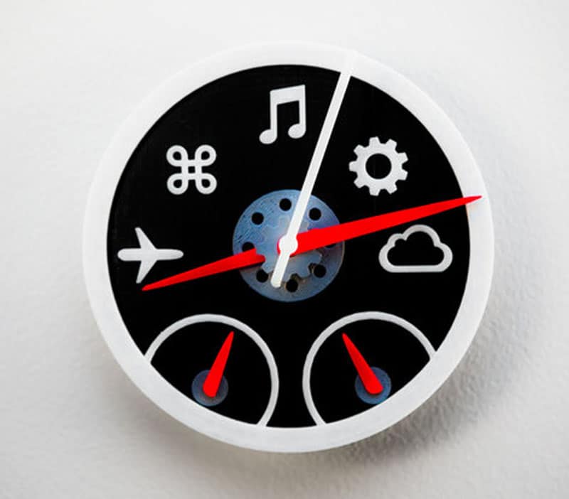 Circular clock icon with black face, white border, and red hands, featuring various white icons including airplane, music note, cloud, and gear.
