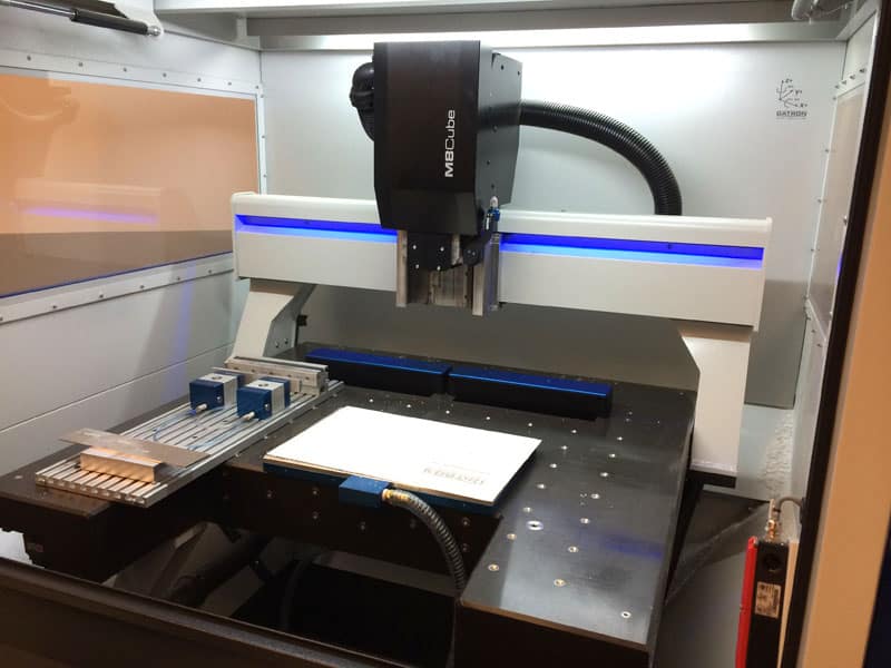 A large 3D printer in a workshop setting with blue lights and components.