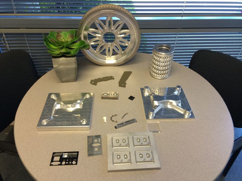 Precision-machined aluminum parts on a round table near a window with blinds.