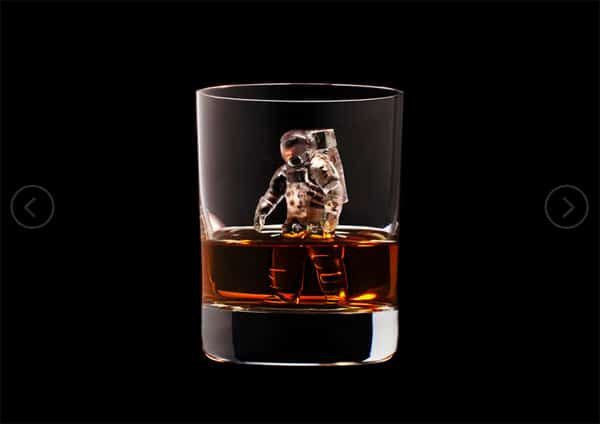 A glass of whiskey with an astronaut figurine on a black background.