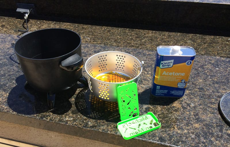 A black pot sits on top of a granite countertop next to a stainless steel basket filled with yellow liquid.