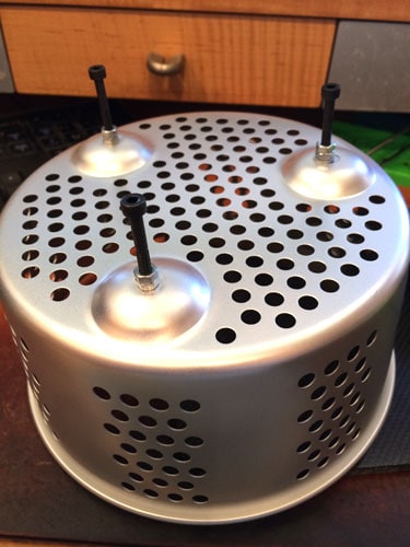 A silver metal basket with perforations and two black plastic feet.