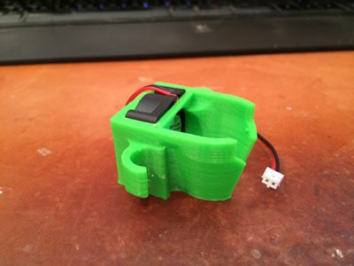 Small green plastic component with black square and red wire.
