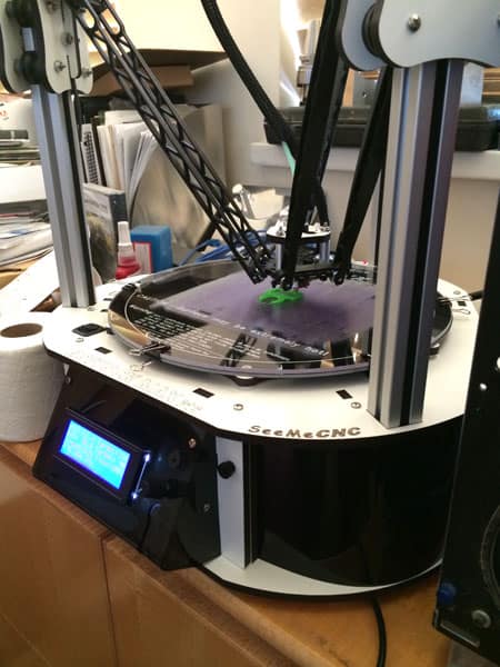 3D printer with white body, black accents, flatbed, and green filament.