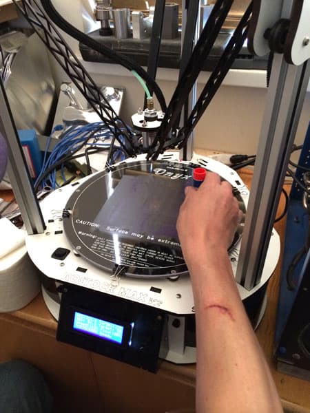 A person's arm with a red glue stick attached, in a workshop setting with machinery and tools.