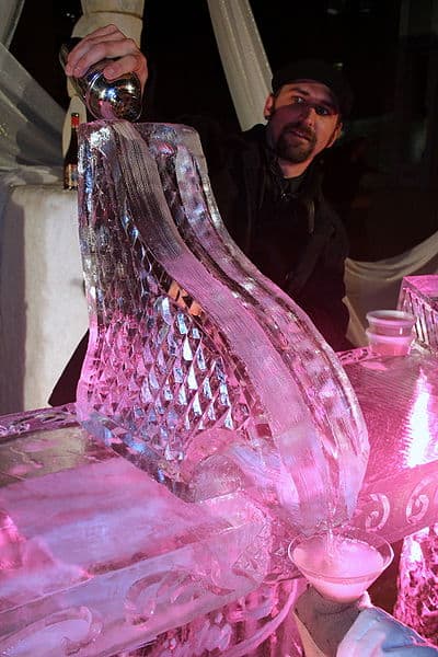 Man standing behind a martini-shaped ice sculpture with diamond pattern and a small cup beside it.