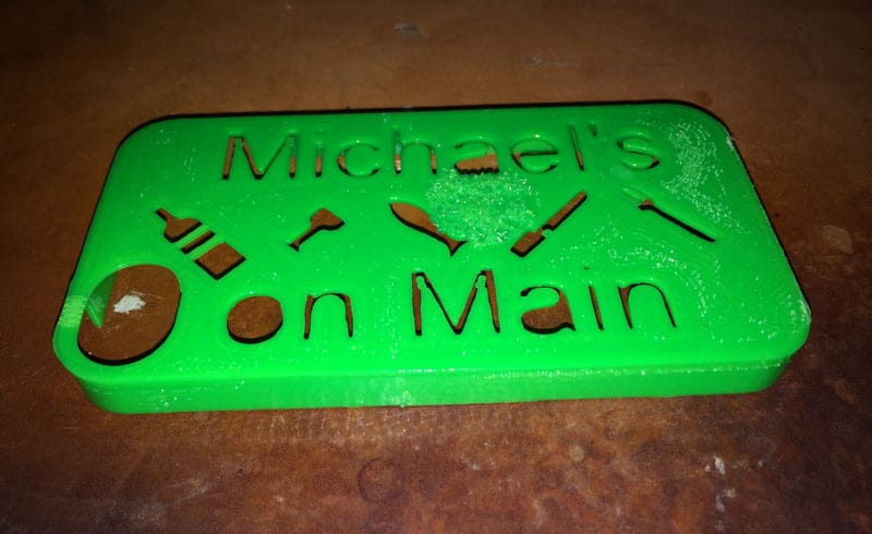 A green plastic sign with the words 'Michael on Main' and icons of a bottle, knife, and spoon.