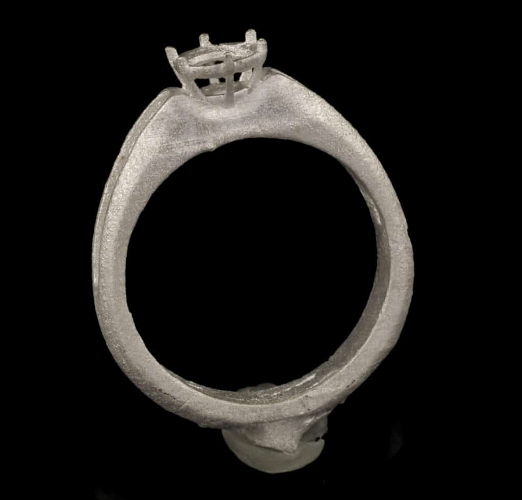 Silver ring casting mold with textured surface and black background.